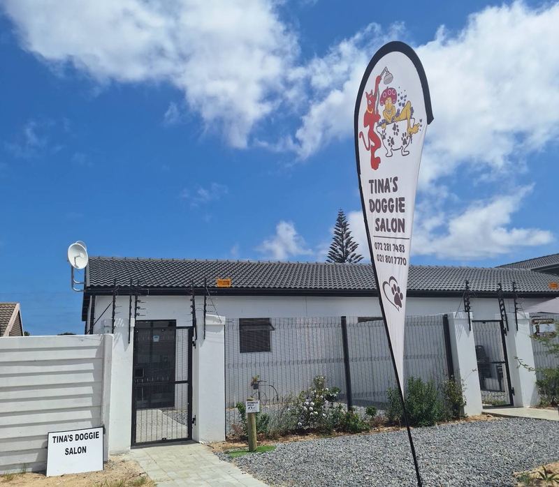 Tina's Doggie Salon in Bothasig: a white single-storey salon with a black roof, a gated front path and the salon's flag out front